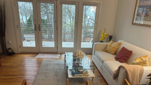 A living room with a white sofa, a glass coffee table, and a patterned rug. - Bright and Spacious Summer Home Steps from the Beach (Shelter Island)