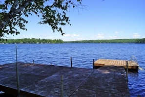 A wooden dock extending into a calm lake with a forested shoreline in the background. - House in exceptional condition on Thomas Pond (Casco)