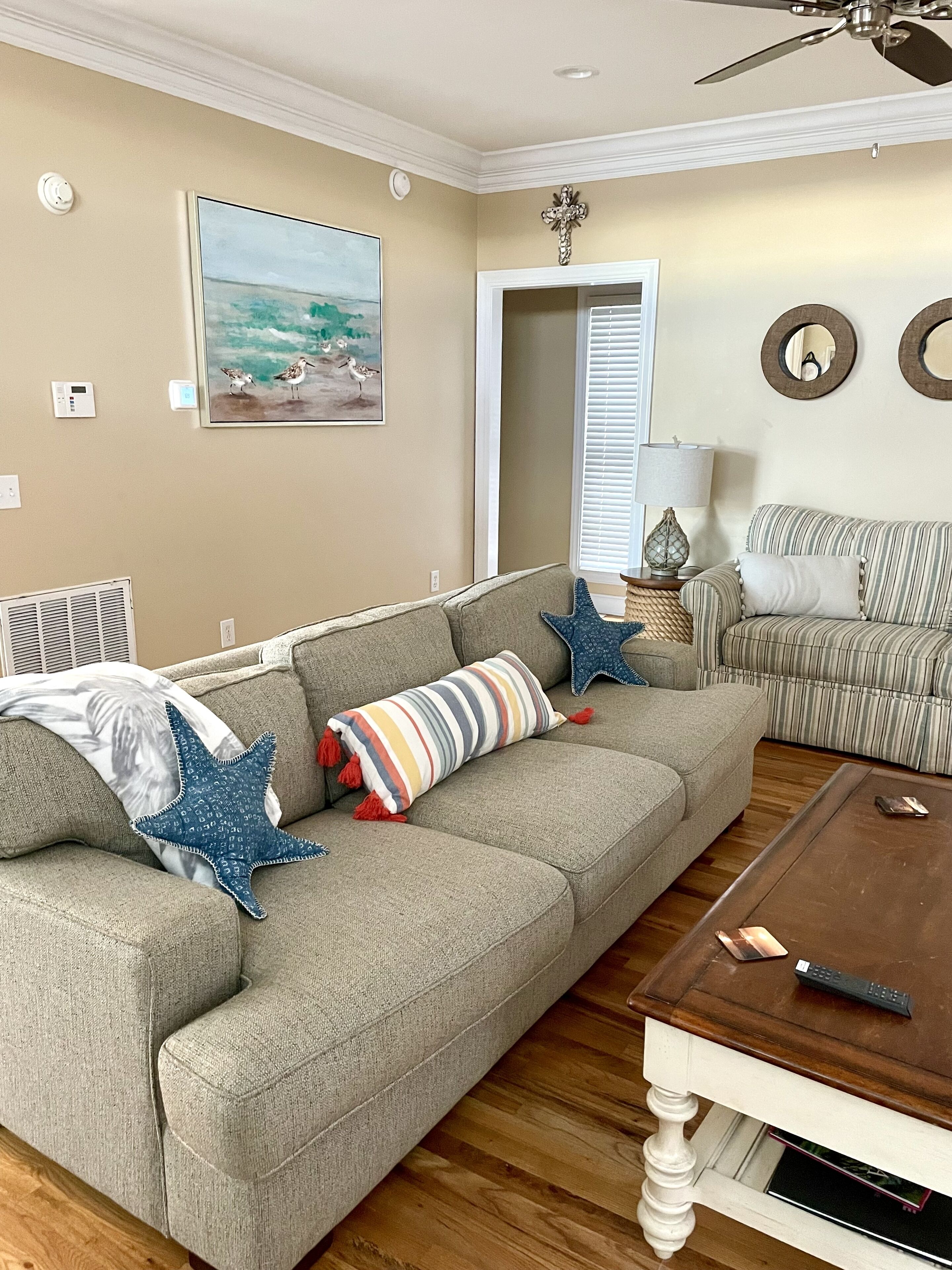 A living room with a gray sofa, striped pillows, starfish cushions, a wooden coffee table, and a painting of birds on the wall.