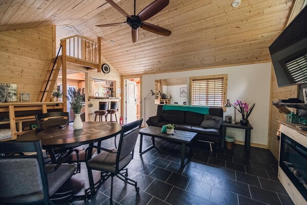 A cozy cabin interior with a dining area, a sofa, and a fireplace.