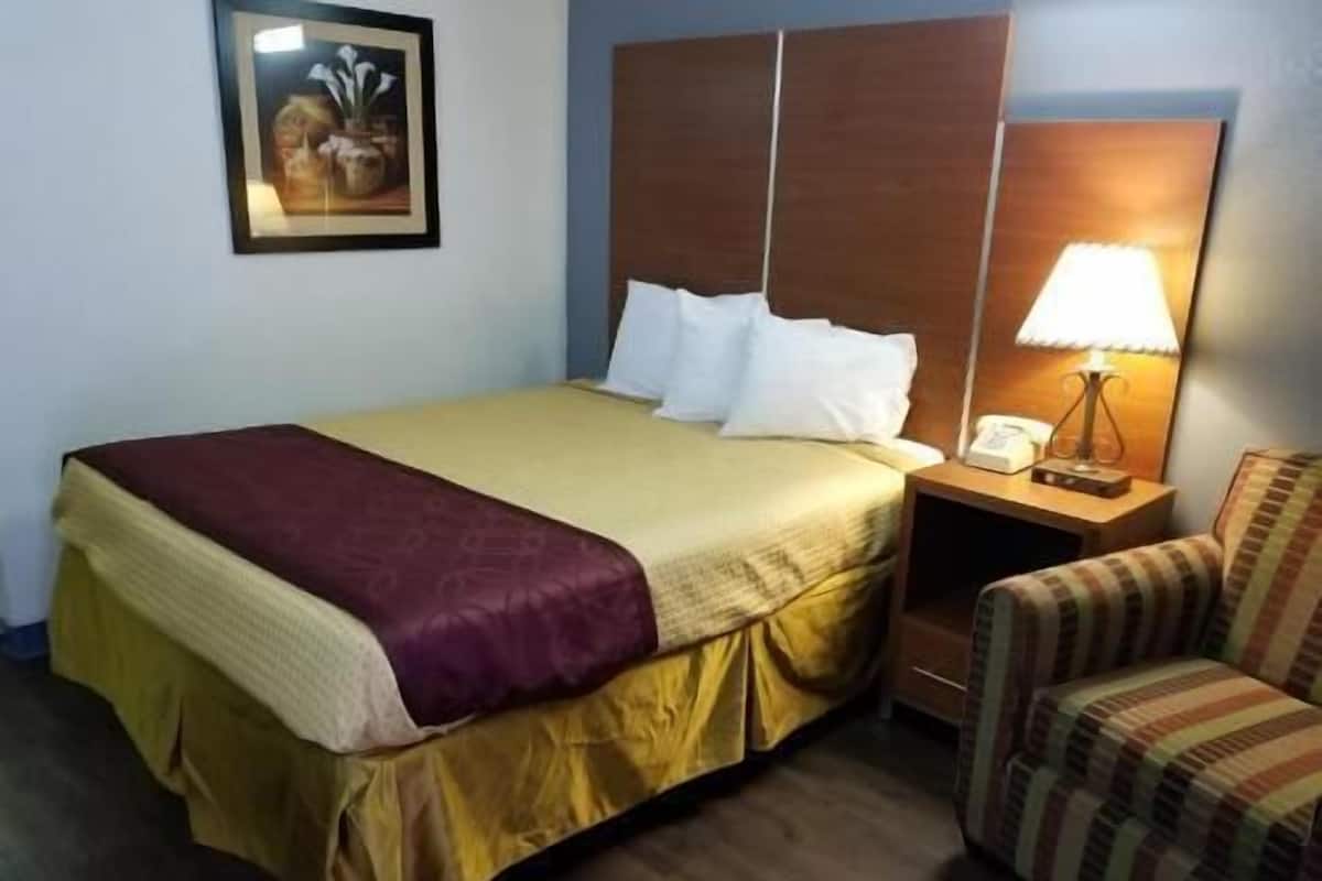 Une chambre d’hôtel avec un lit, une table de chevet avec une lampe, une chaise et un tableau encadré au mur.