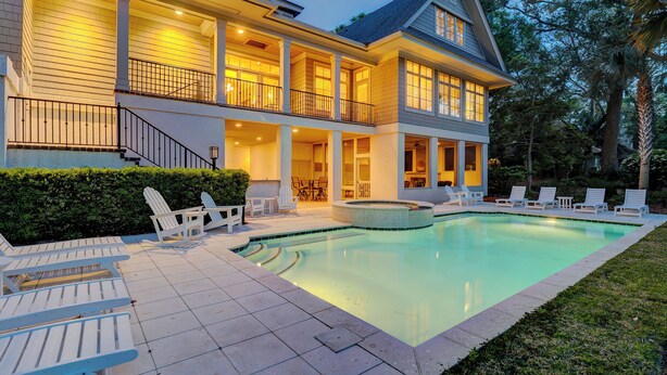 A two-story house with a swimming pool, outdoor seating, and a well-lit patio area. - GORGEOUS 7 Bedroom 2nd Row Ocean Home with Private Pool & Game Room (Hilton Head Island)