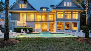 A two-story house with a swimming pool, outdoor seating, and a well-lit balcony. - GORGEOUS 7 Bedroom 2nd Row Ocean Home with Private Pool & Game Room (Hilton Head Island)