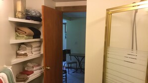 A room with a wooden door leading to a dining area, a trash bin, and shelves with folded towels. - Meadows Mountains and more  (Waterbury)