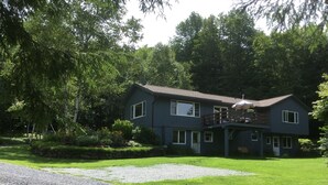 A two-story house with a balcony, surrounded by lush greenery and a gravel driveway. - Meadows Mountains and more  (Waterbury)