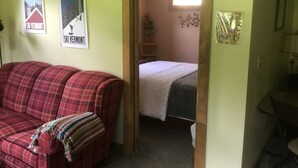 A room with a red plaid couch, a bed with a white blanket, and two posters on the wall. - Meadows Mountains and more  (Waterbury)