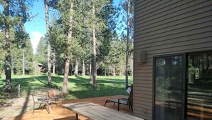 Une terrasse en bois avec des tables de pique-nique, un espace de repos abrité et une vue sur une zone boisée.