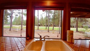 Une salle de bain avec un lavabo et une vue sur un terrain de golf, grâce à de grandes fenêtres.