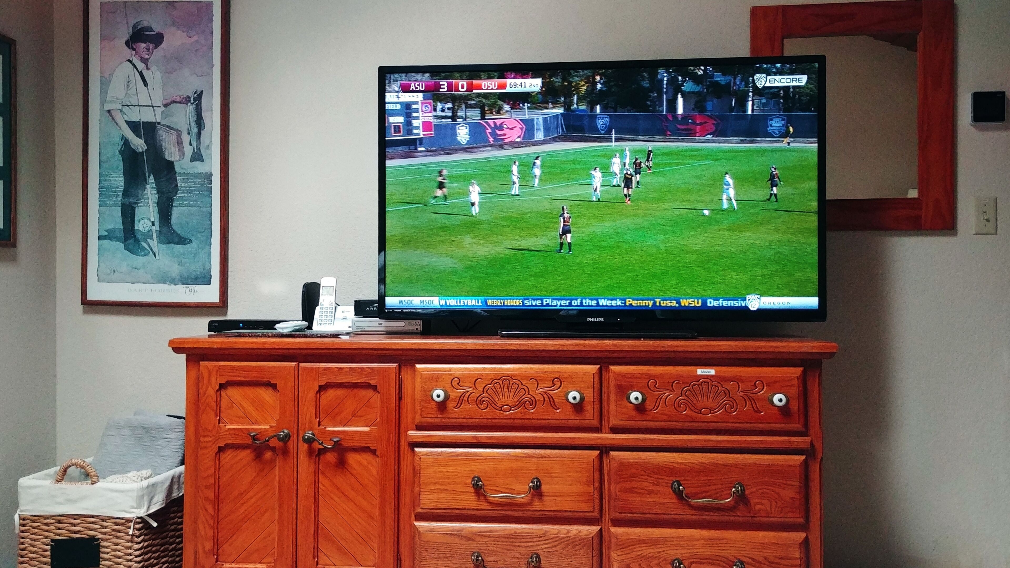Televisor que mostra un partit de voleibol, muntat sobre un moble de fusta amb calaixos.