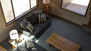 Un salon avec un canapé gris, des coussins à motifs, une table basse en bois et une lampe.
