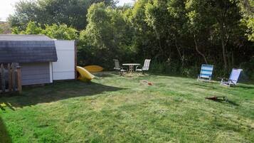 Relax in the serene backyard with a shed, slide, and comfortable lawn chairs surrounded by lush trees.
