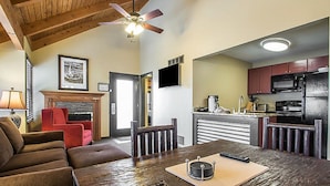 A spacious living area with a wooden ceiling, a fireplace, a dining table, and a kitchen with modern appliances.