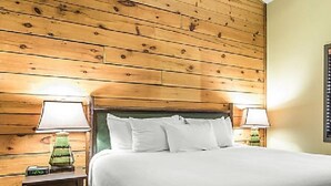 A hotel room with a wooden headboard, a bed with white bedding, two bedside lamps, and a nightstand with a clock.