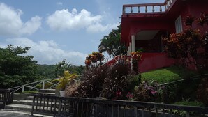 A red building with a balcony, surrounded by lush greenery and a clear sky. - Ridge Bay Chateau (Port Antonio)