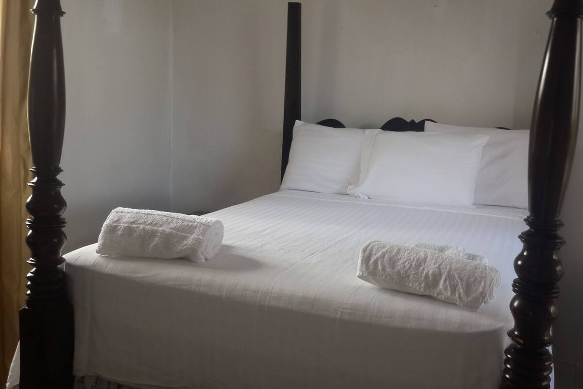 A four-poster bed with white linens and two towels placed on the foot of the bed.