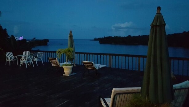 A deck with outdoor seating and a view of the ocean at dusk. - Ridge Bay Chateau (Port Antonio)