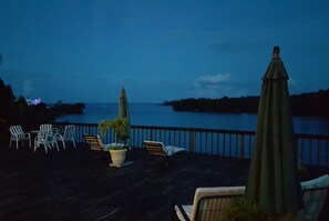 A deck with outdoor seating and a view of the ocean at dusk.
