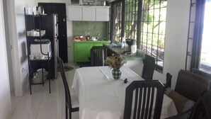 A dining area with a table set for two, a vase with dried flowers, and a kitchen in the background. - Ridge Bay Chateau (Port Antonio)