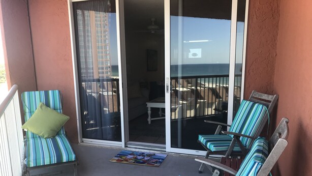 Un balcon avec deux fauteuils de jardin à rayures, dont l’un est agrémenté d’un coussin vert, et une petite table avec un set de table coloré.