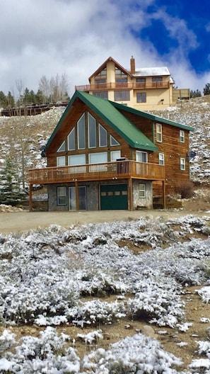 A two-story wooden cabin with a green roof, a balcony, and a stone foundation.