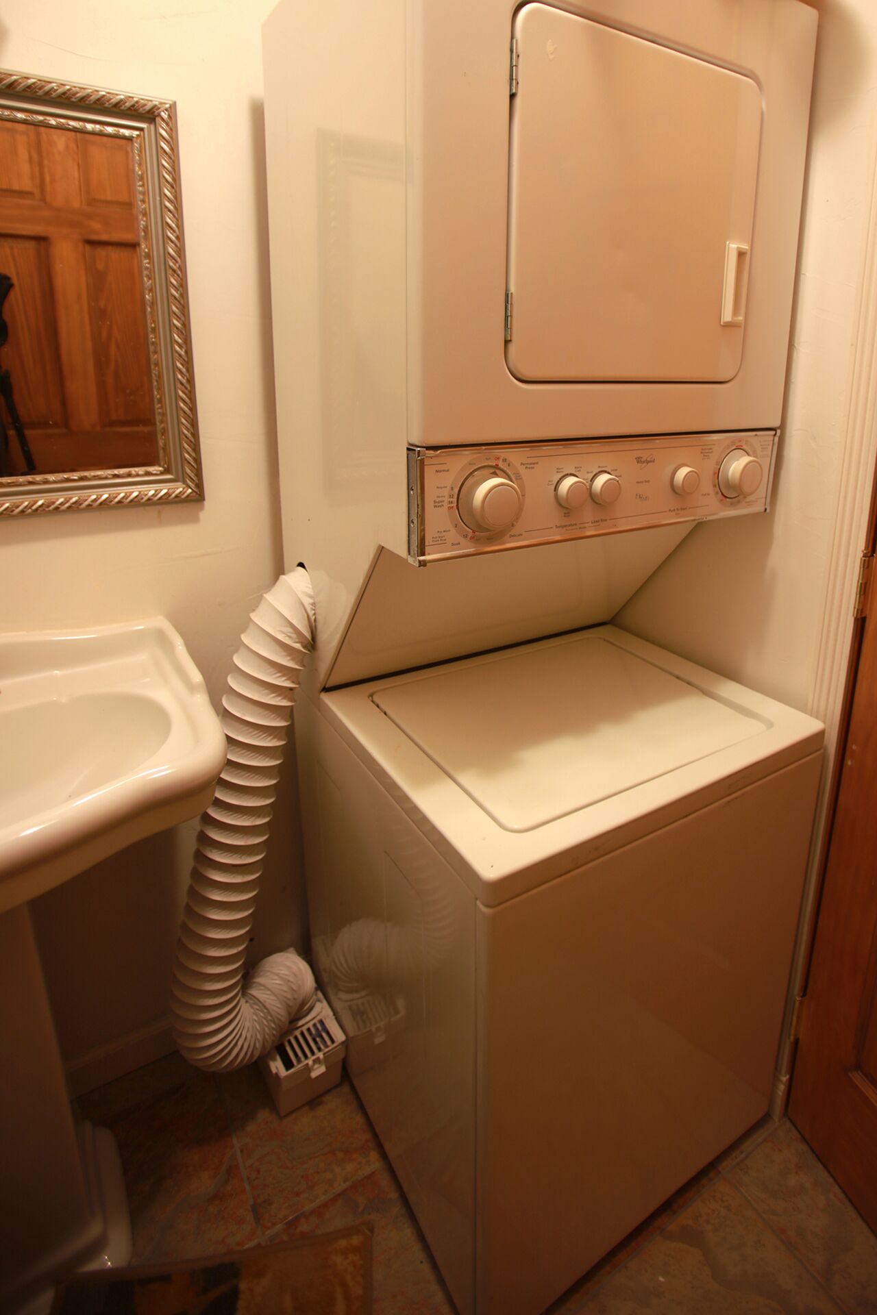 A compact washer and dryer unit in a small bathroom with a sink and a mirror.