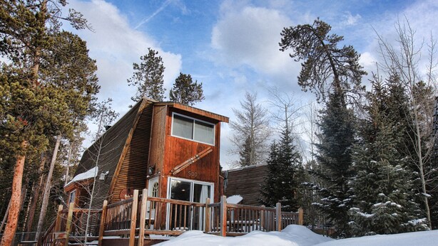 A wooden cabin with a large window and a deck, surrounded by snow and trees. - Cabin in Breckenridge  - Walk to Main Street & Peak 9 Lifts (Breckenridge)