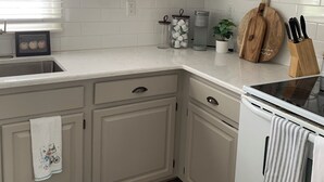 Een keuken met witte kastjes, een fornuis, een spoelbak en een raam met jaloezieën.