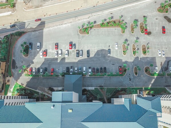 An aerial view of a parking lot with multiple rows of parked cars and landscaped areas with trees.