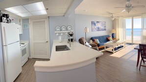 Una cocina moderna con una isla integrada, un comedor con mesa y sillas, un sofá y vistas al océano a través de amplios ventanales.