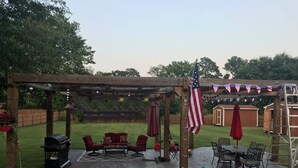 Un área de patio techada con una parrilla, muebles de patio rojos y una bandera estadounidense.