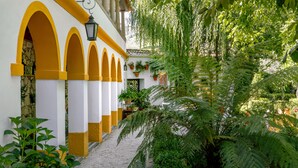Um pátio com paredes brancas e amarelas, arcos e plantas em vasos.