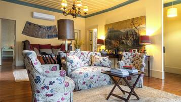 A living room with floral upholstery, a chandelier, and a painting on the wall.