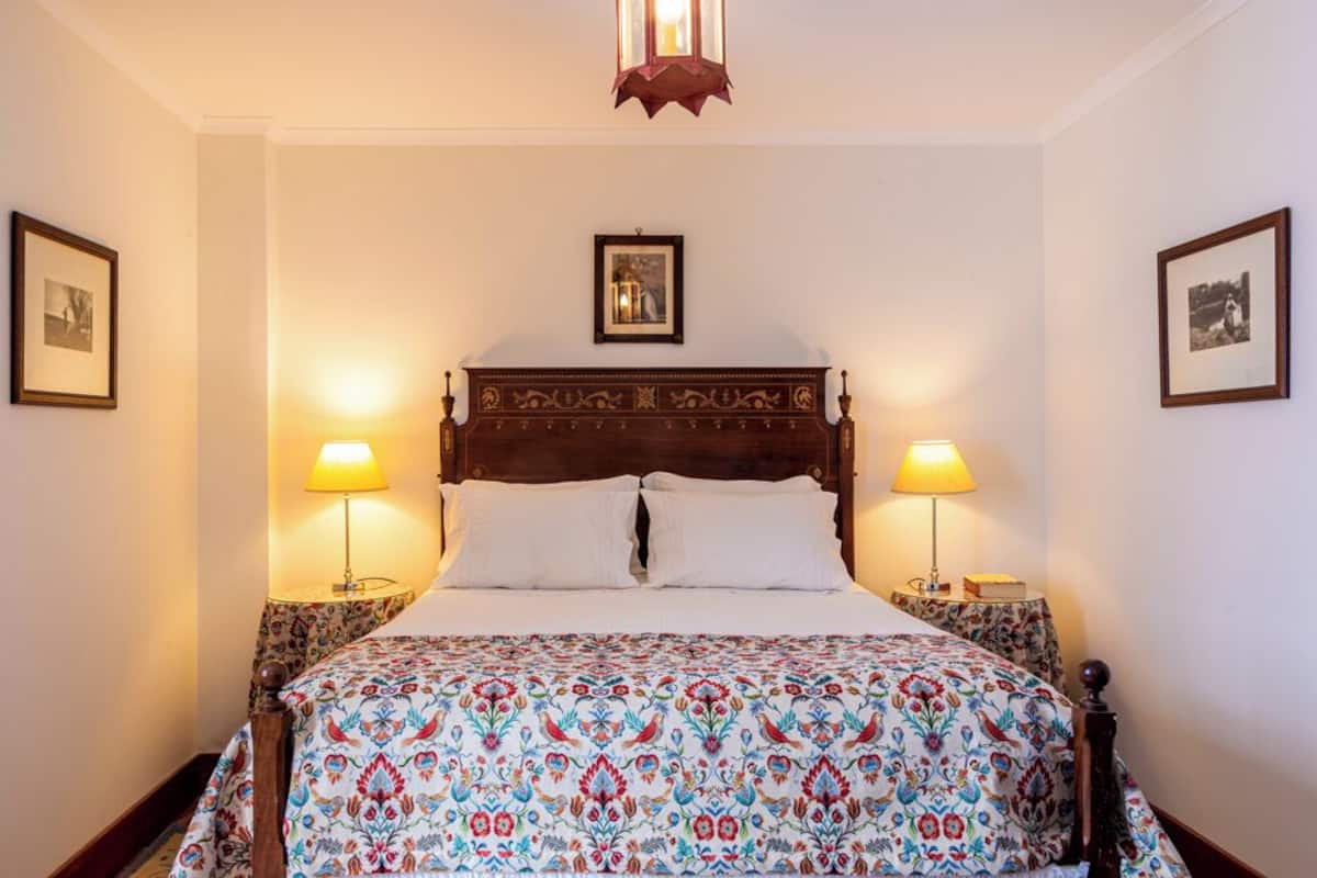 A bed with a patterned bedspread, two bedside lamps, and framed pictures on the walls.