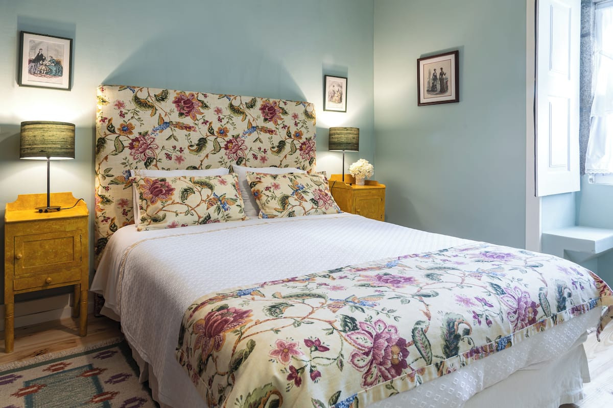 A bedroom with a floral bedspread, two bedside lamps, and framed pictures on the wall.