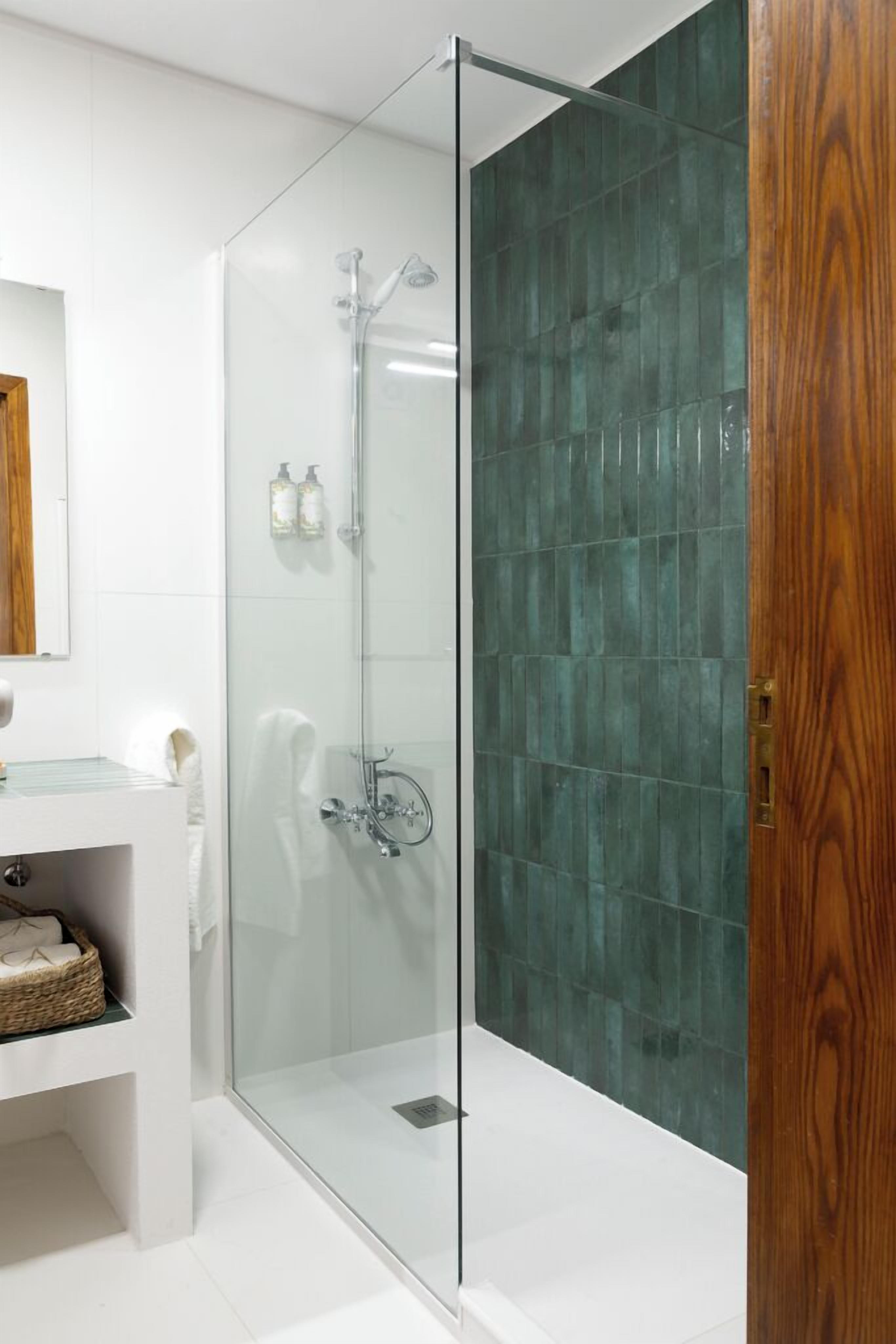 A modern bathroom with a glass-enclosed shower, white tiles, and a wooden door.