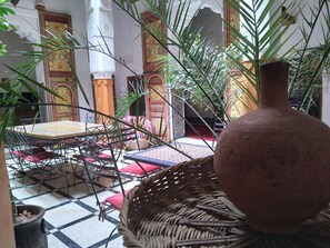 Un interior tradicional amb un terra de quadres, una taula rodona i cadires amb coixins vermells.