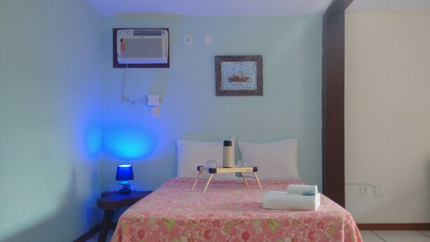 A hotel room with a bed, a bedside table with a lamp, a picture on the wall, and a thermostat. - Biruta Guest House (Búzios)