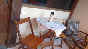 A small wooden table with a lace tablecloth and a thermos. There are two wooden chairs with cushions. - Biruta Guest House (Búzios)