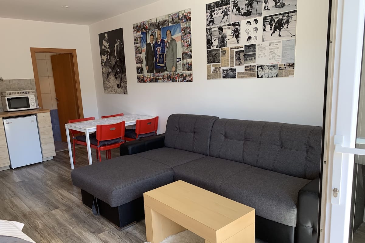 Uma sala de estar moderna com um sofá seccional cinza, uma mesa de madeira pequena e uma área de jantar com cadeiras vermelhas.