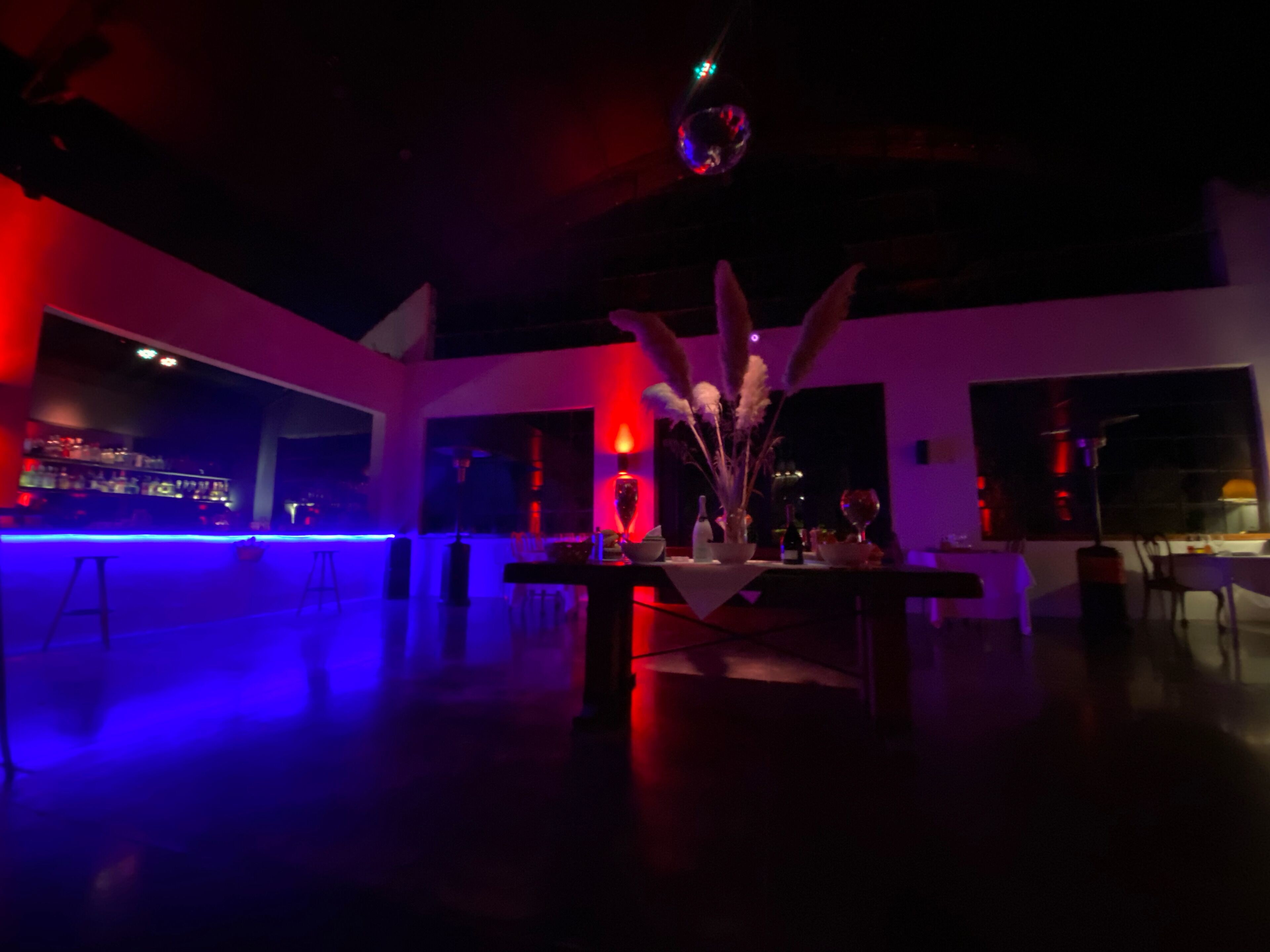 A dimly lit bar area with a modern interior, a bar counter, and a seating area with tables and chairs.