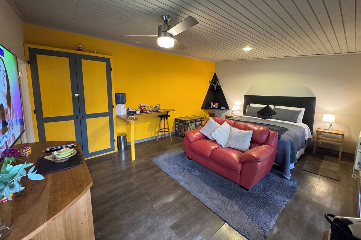 Una habitación con una cama, un sofá de cuero rojo, una pequeña zona de bar y un ventilador de techo.