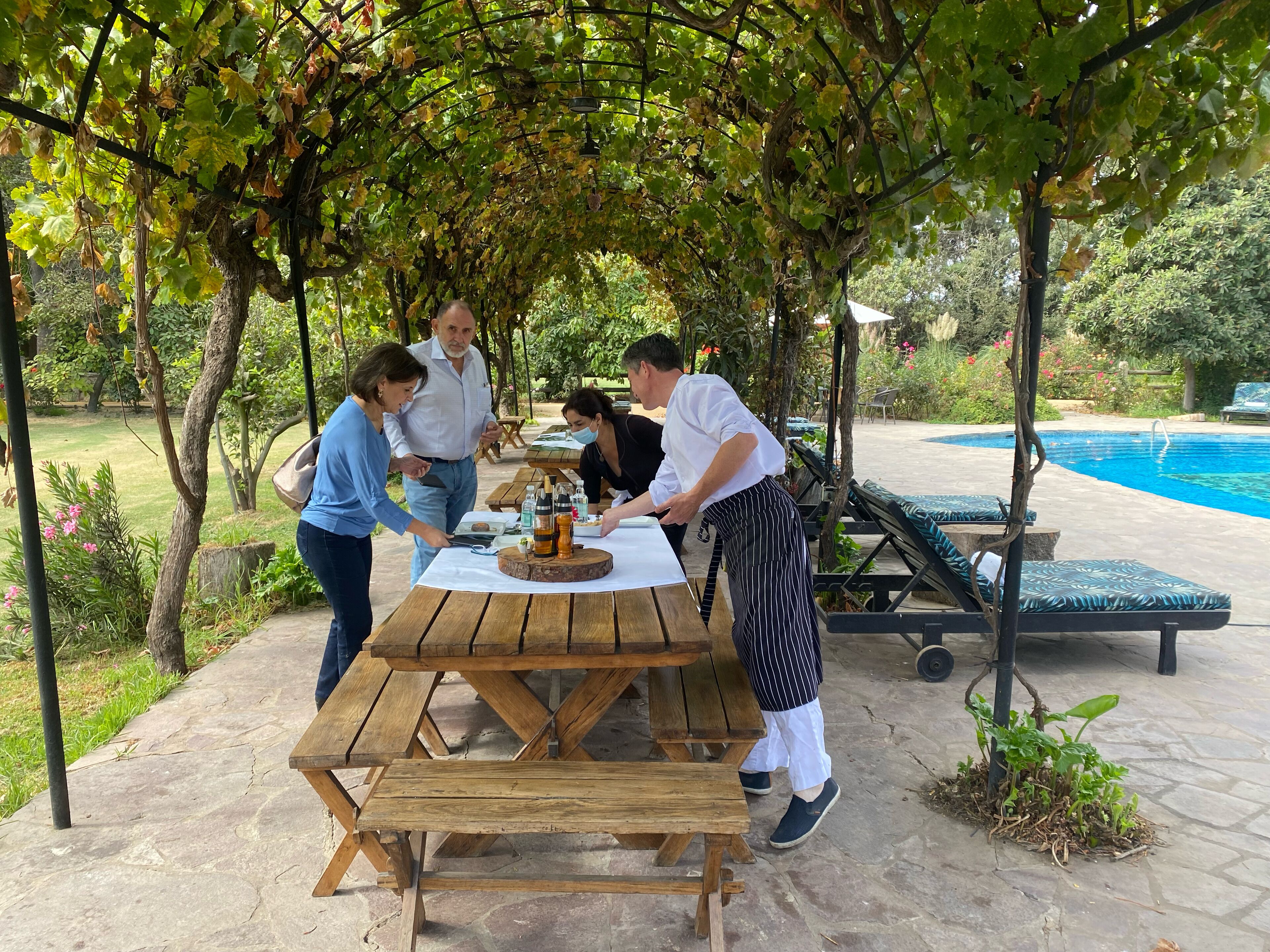 A wooden picnic table with a bottle of wine, surrounded by people.
