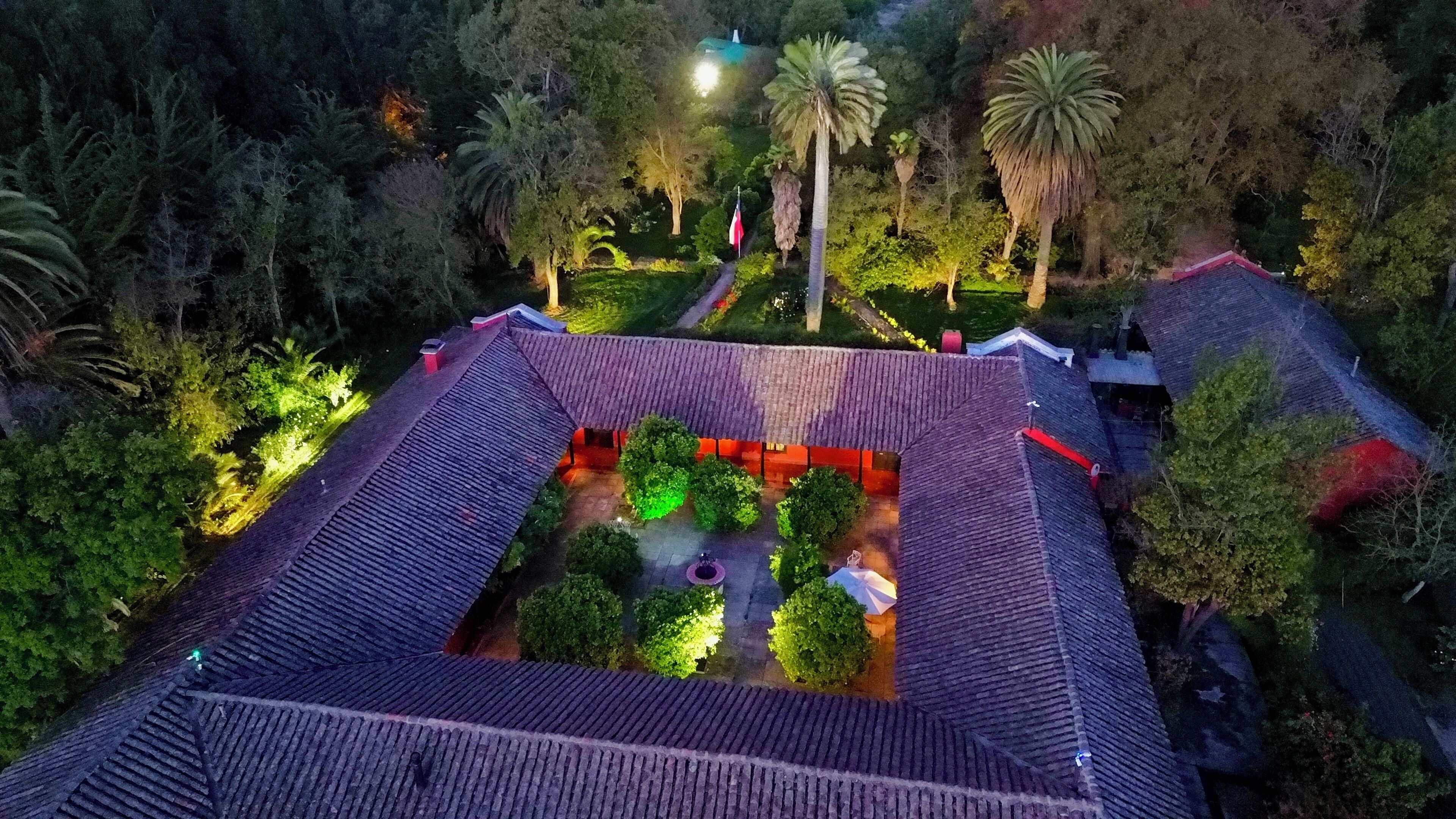 An aerial view of a traditional building with a tiled roof, surrounded by lush greenery and palm trees.