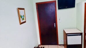 Une pièce avec une porte en bois, une petite armoire blanche, un tableau encadré accroché au mur et un téléviseur fixé au-dessus de la porte.