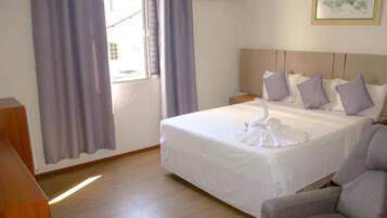 A hotel room with a bed, a nightstand, a chair, a window with curtains, and an air conditioning unit.