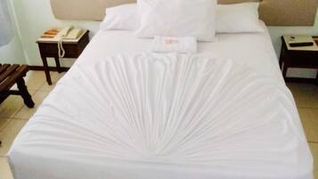 Uma cama bem arrumada com cabeceira estofada, roupa de cama branca e uma pequena mesa de cabeceira com um telefone e um livro.