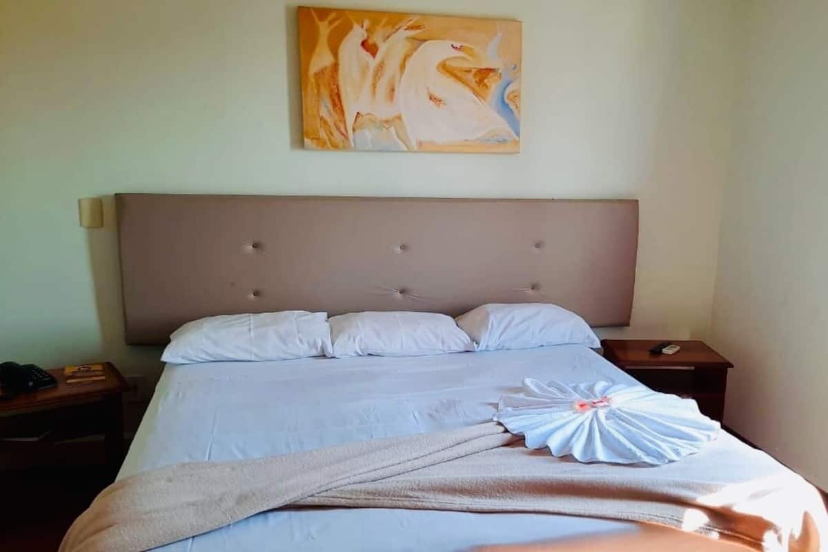 Un llit ben fet amb una tovallola i un objecte decoratiu, un panell frontal, una tauleta de nit amb un telèfon i un quadre a la paret.