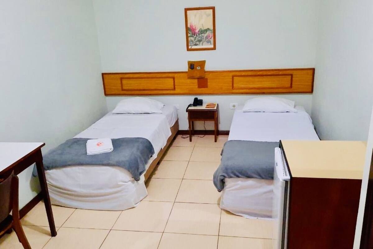 Habitació amb dos llits individuals, una taula petita, una cadira i una taula de nit amb una làmpada.