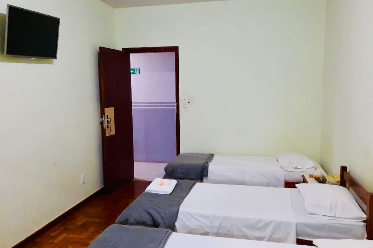 Habitació petita i senzilla amb dos llits, una televisió i una porta que dona a un passadís.