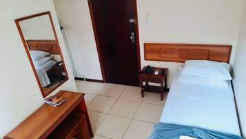 Habitación de hotel con cama de madera, mesita de noche con teléfono y lámpara, pequeño escritorio con silla y espejo en la pared.